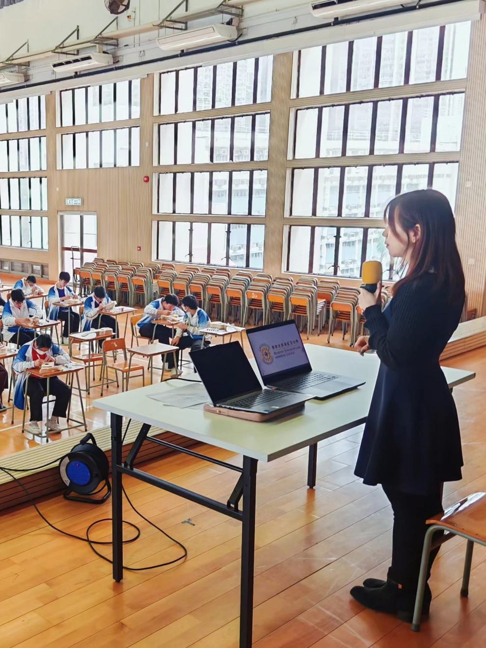 Ms Rita 手持咪高峰於禮堂講解